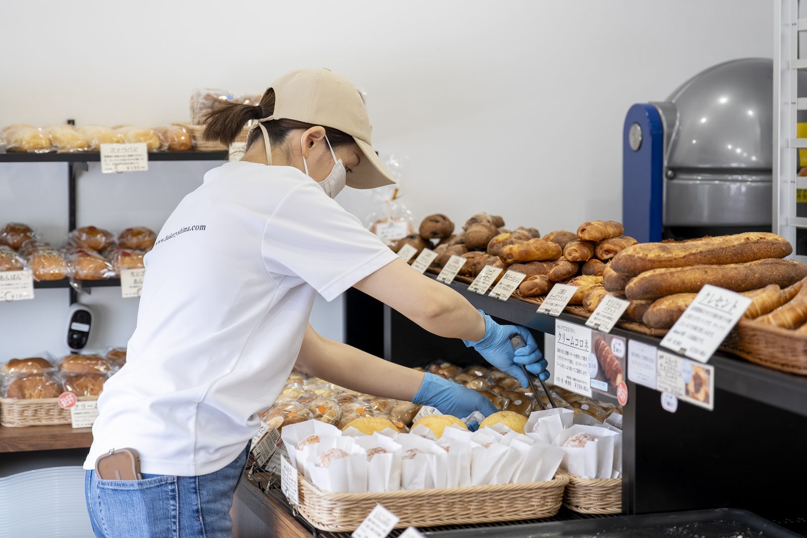 トングで売場のパンを品出しするスタッフ
