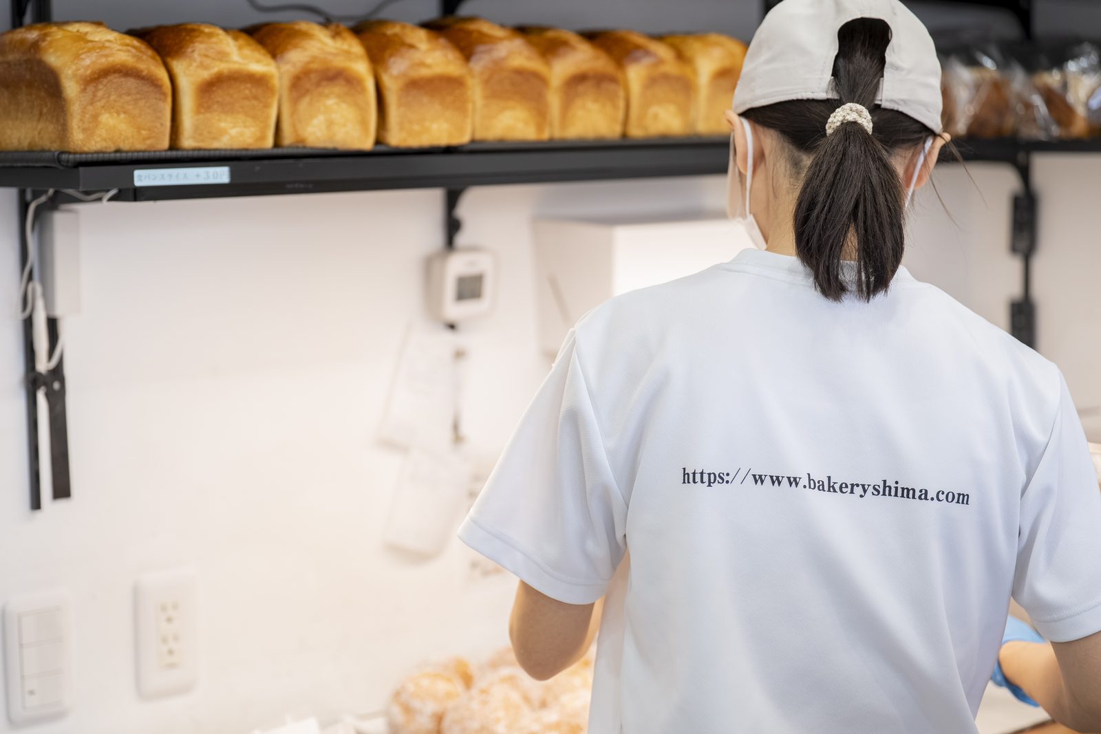 食パンが並ぶ棚と、shimaの制服を着て働くスタッフの後ろ姿