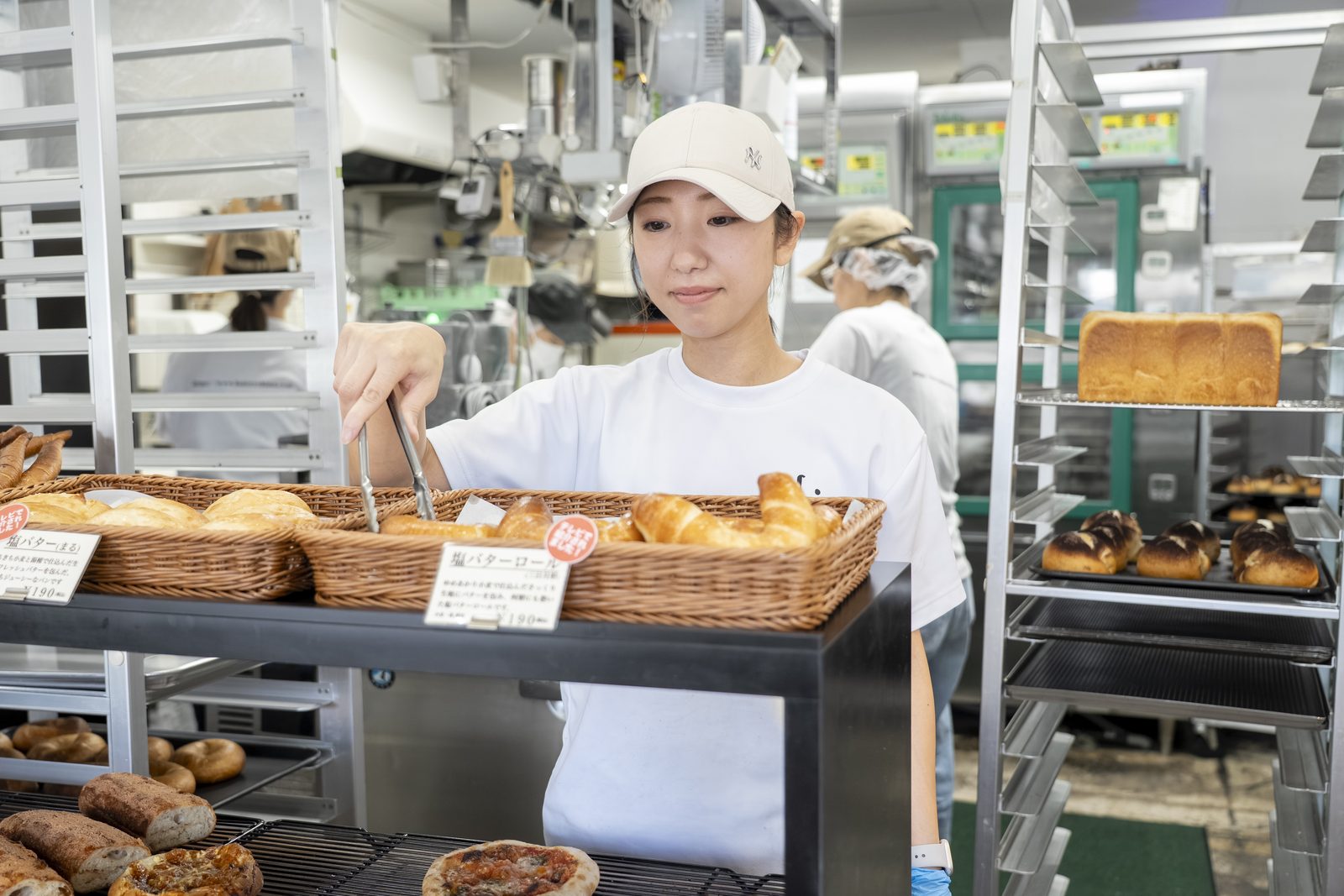 トングでパンを品出しするスタッフ